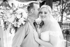 A black and white wedding photo of a couple sharing a tender moment outdoors with a floral arrangement nearby.