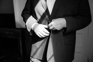 A close-up black and white shot of someone buttoning a formal suit jacket.