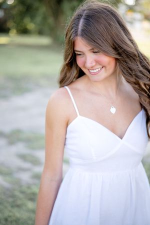 A woman in a white summer dress smiles while looking down in an outdoor portrait series.