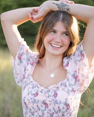 A woman in a floral print dress poses outdoors in golden sunlight during a photo session.