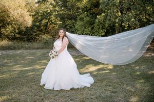 A flowing white wedding dress with a dramatic long veil catches the breeze in an outdoor garden setting.