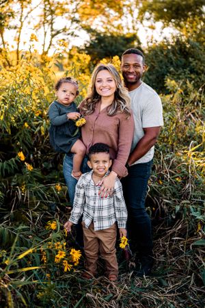 A loving family poses together surrounded by blooming yellow flowers in an outdoor garden setting.