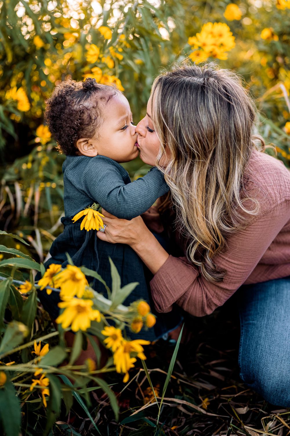 A tender kiss shared between two people in a garden of vibrant yellow flowers during golden hour.