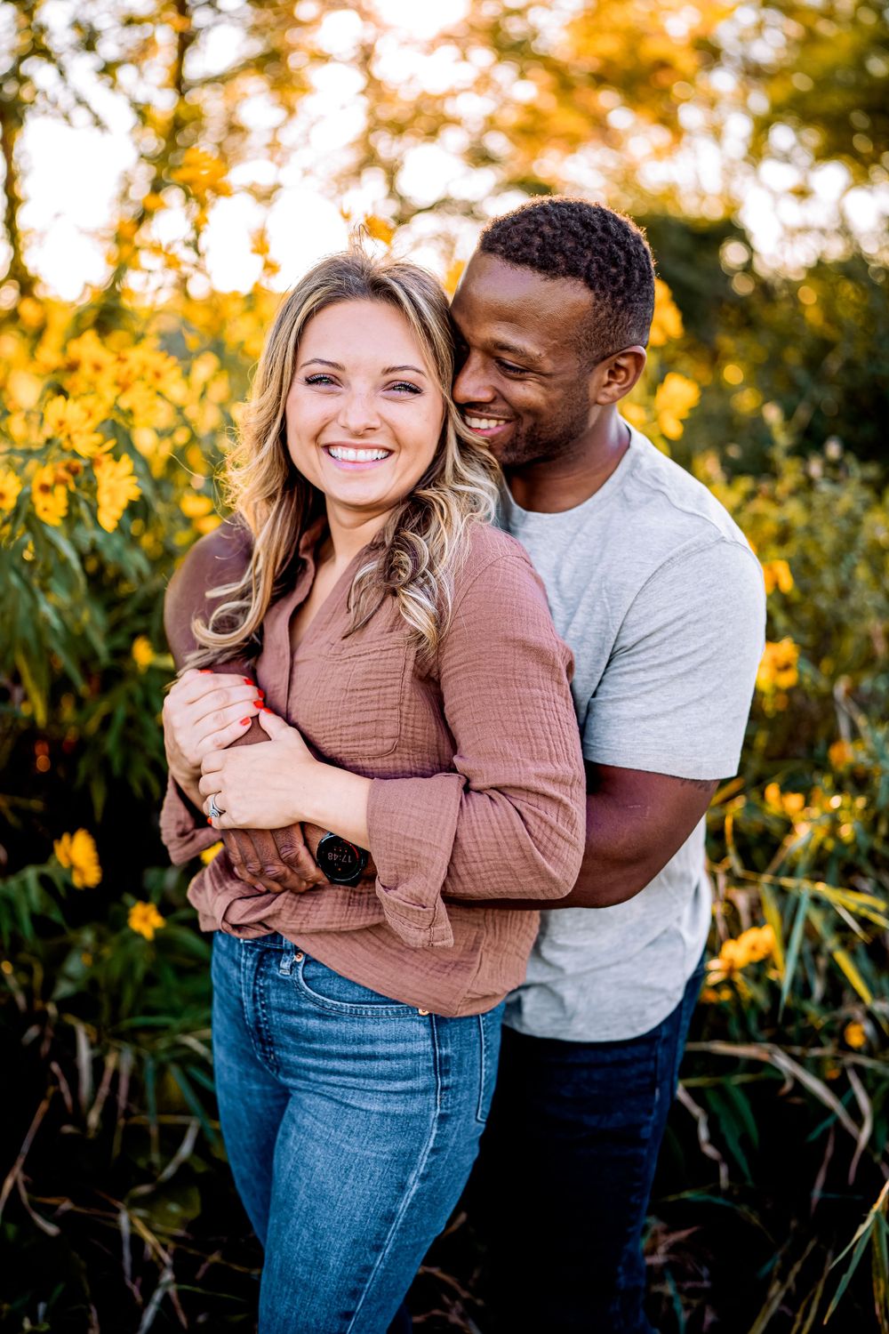 A couple embraces and laughs together among yellow wildflowers during sunset.