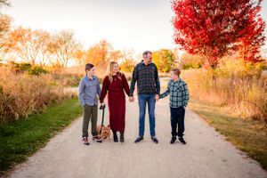A family stands together on a path with vibrant red autumn trees in the background.