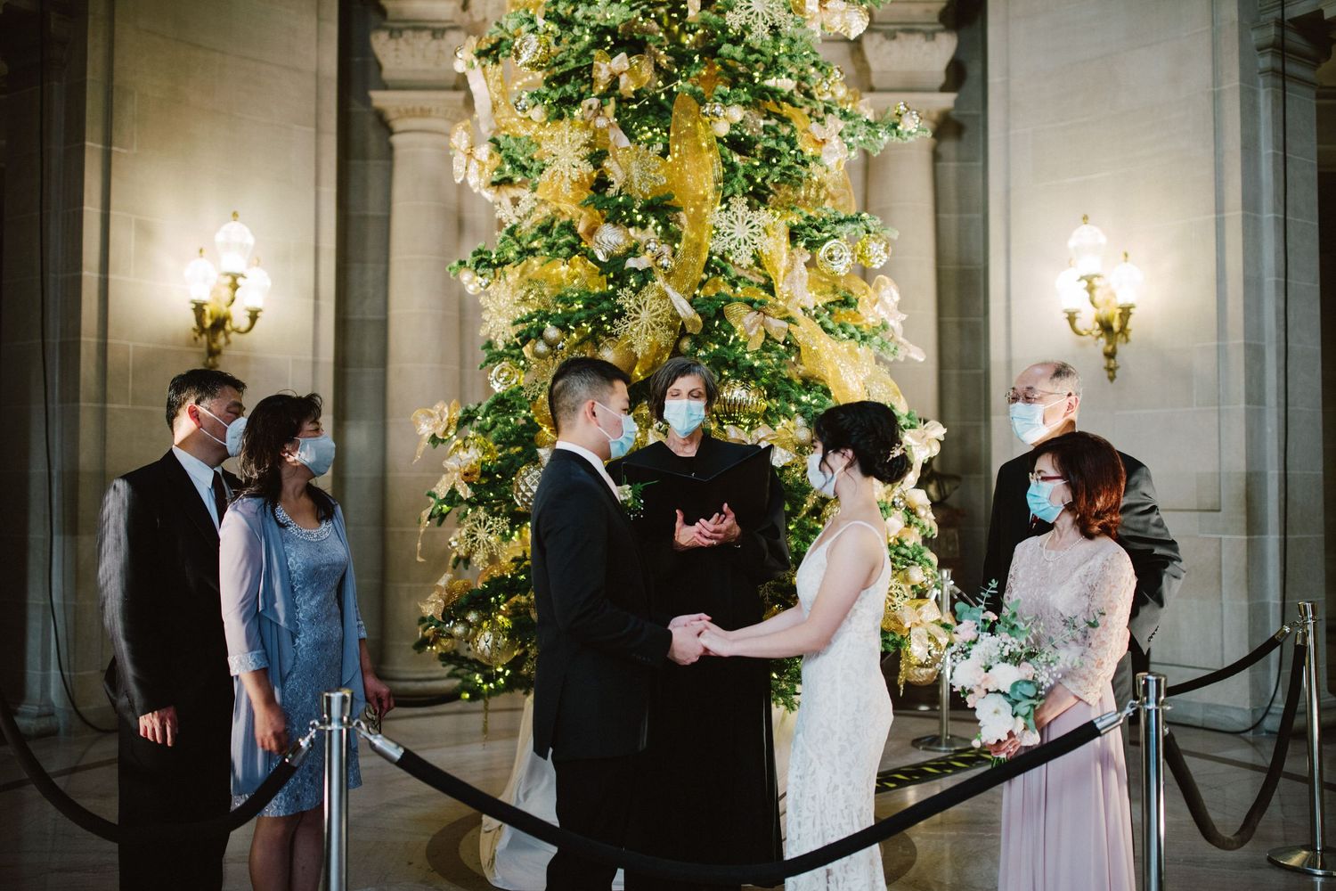 Wedding ceremony in front of decorated Christmas tree with guests in attendance.