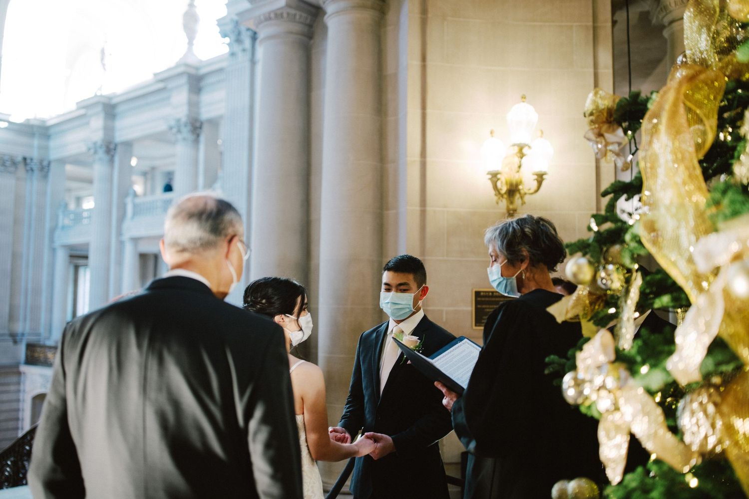 Small group gathered for an intimate indoor wedding ceremony with decorative columns and holiday decor.