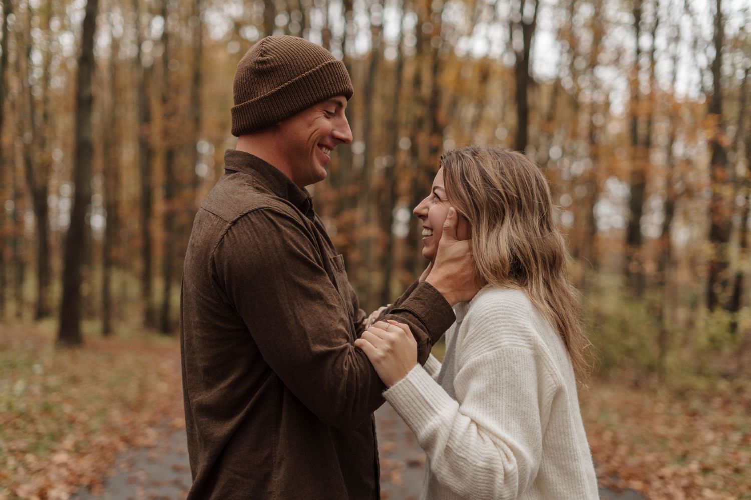 Couple sharing laughter in an autumn forest wearing cozy sweaters.