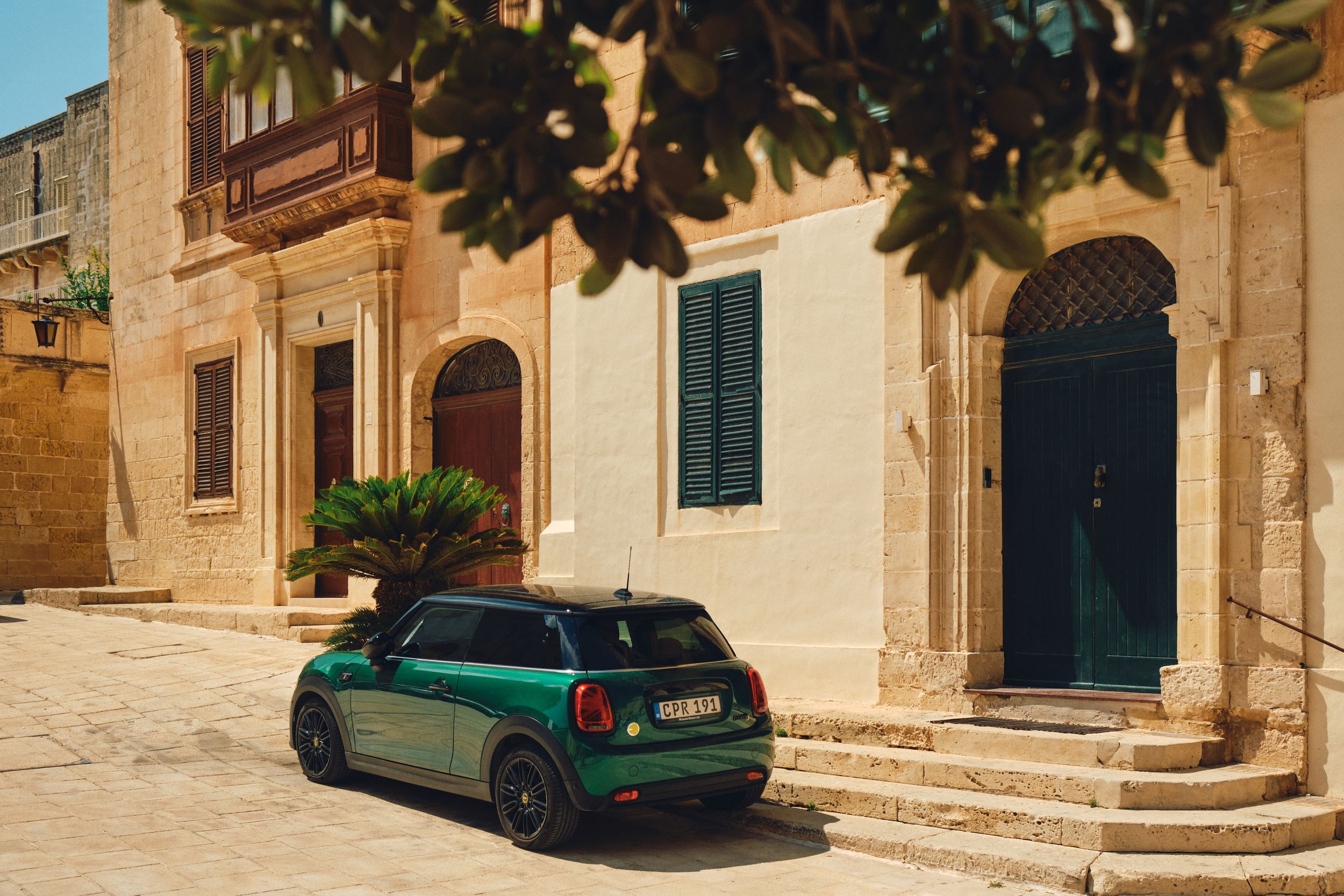 Green Mini Cooper parked in front of traditional Maltese limestone building with blue door.