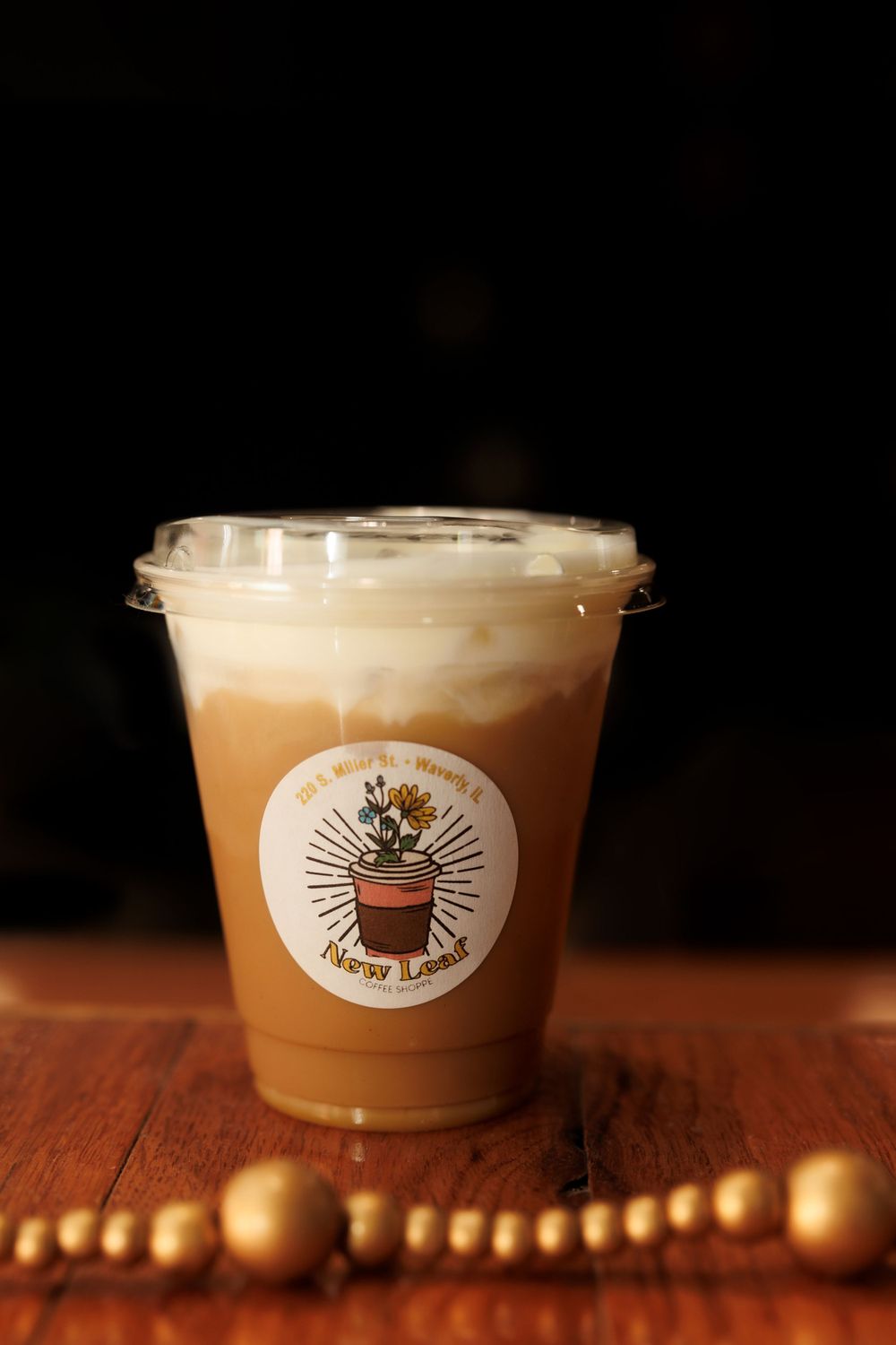 Creamy iced coffee beverage with plant logo on wooden table with gold beaded decor.