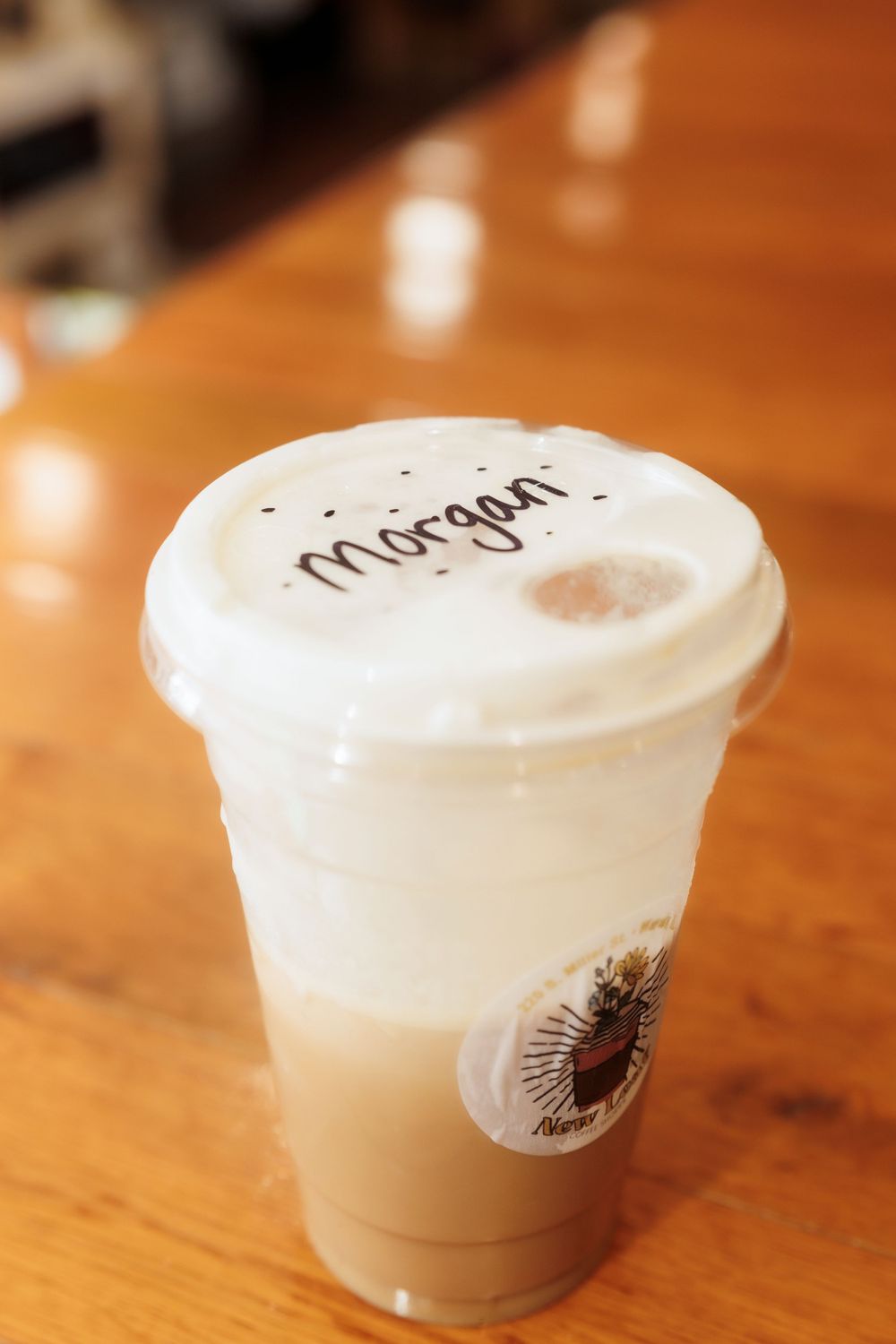 A personalized coffee cup marked 'Morgan' with frothy milk top on wooden table.