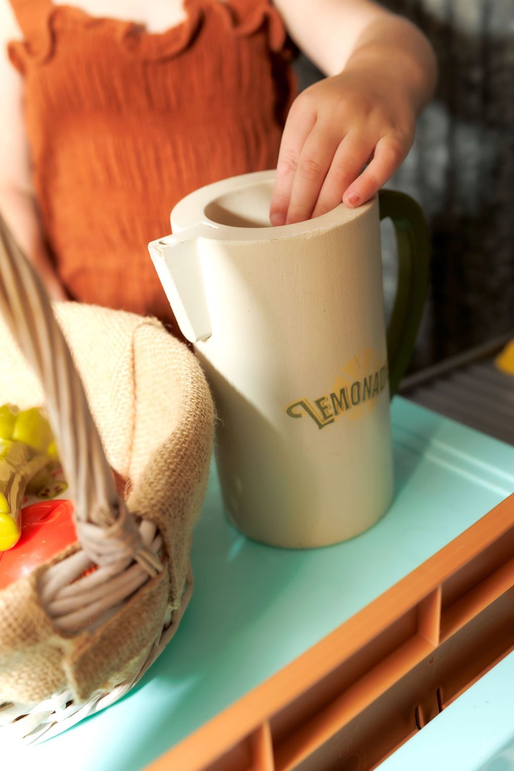 Hand reaching for ceramic lemonade pitcher on turquoise shelf.