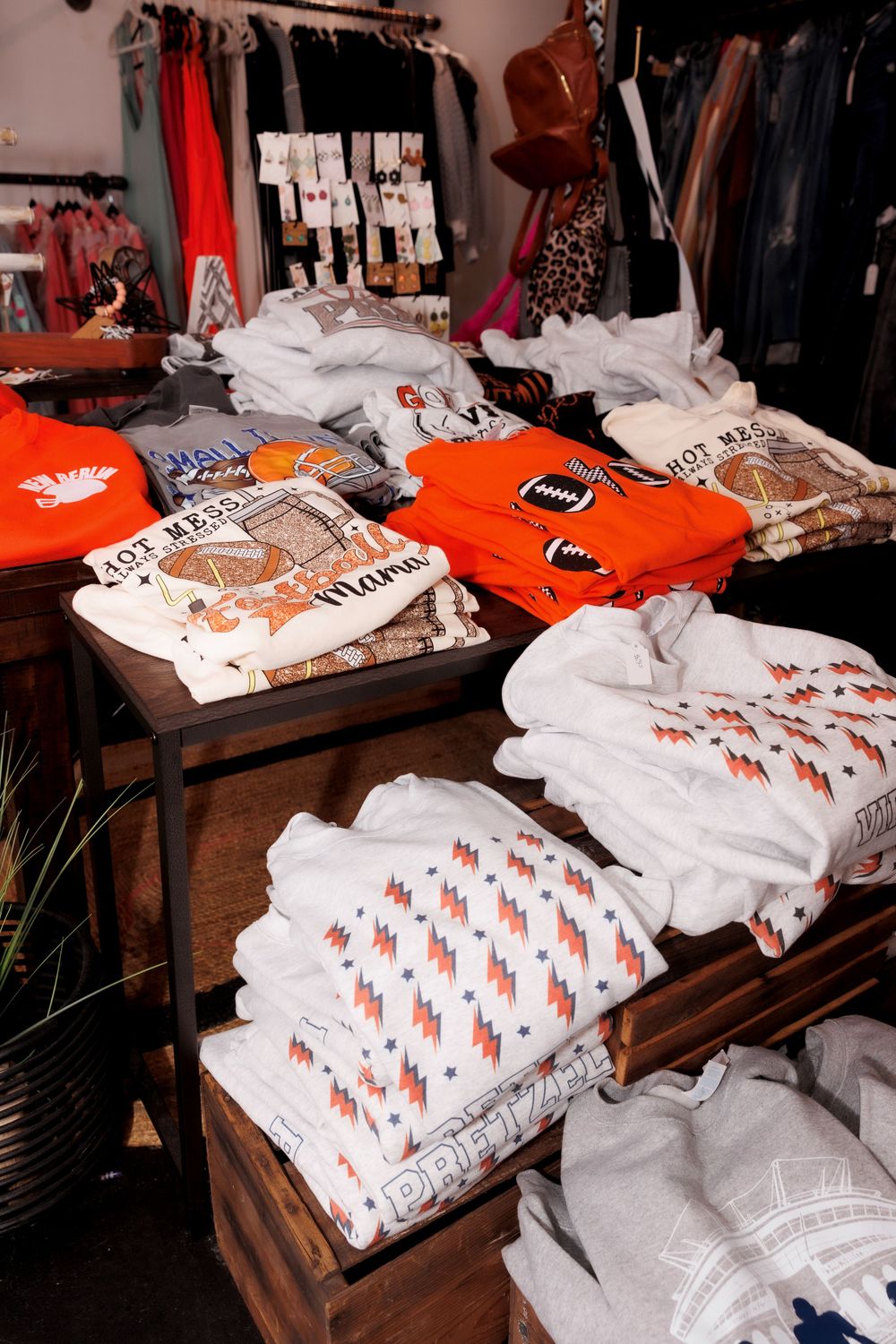Retail display of folded t-shirts in orange and white with graphic designs.