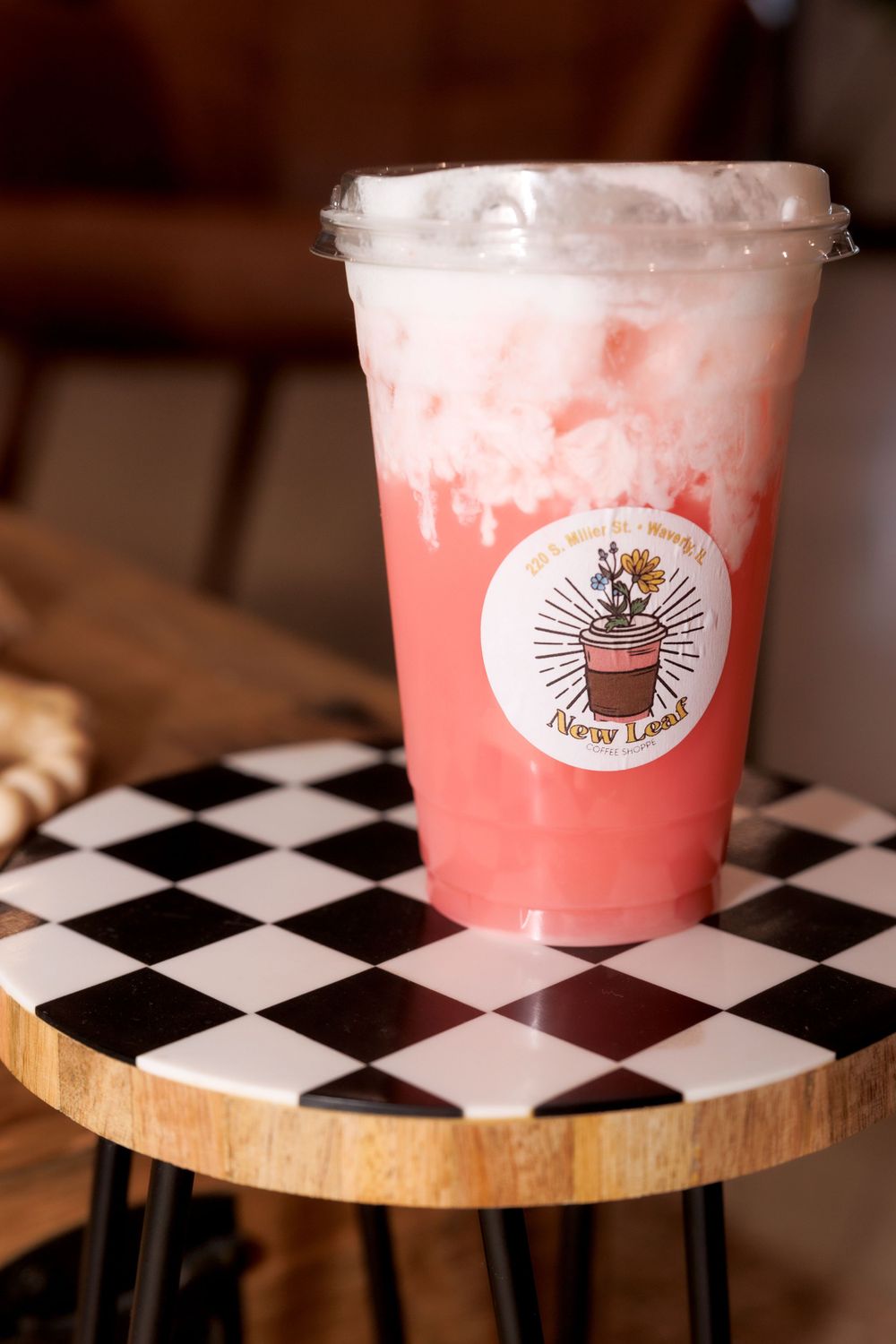 Pink fruity drink in clear plastic cup on checkered wooden table surface.
