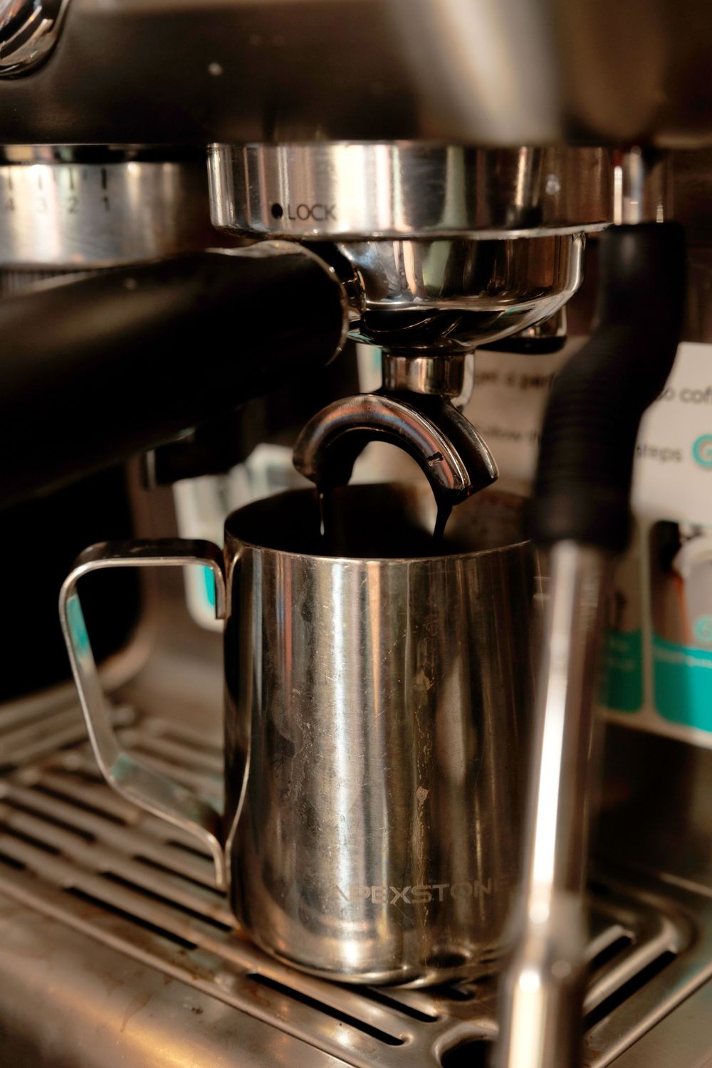 Stainless steel milk pitcher under an espresso machine spout.