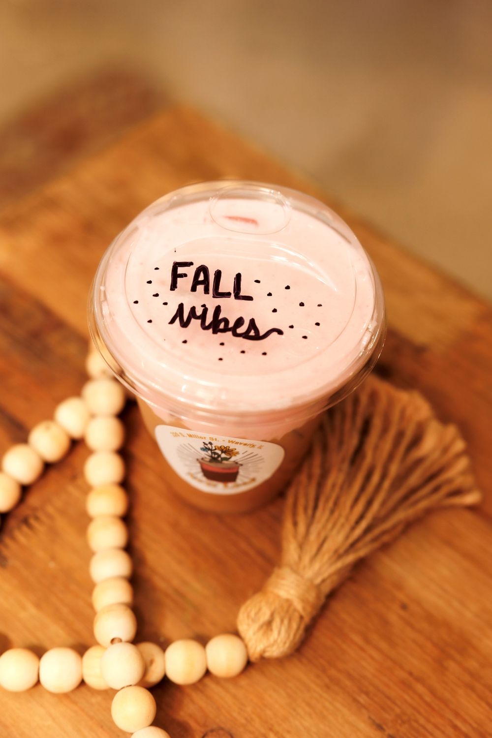 Fall vibes coffee drink with wooden beads and tassel decoration on wooden table.