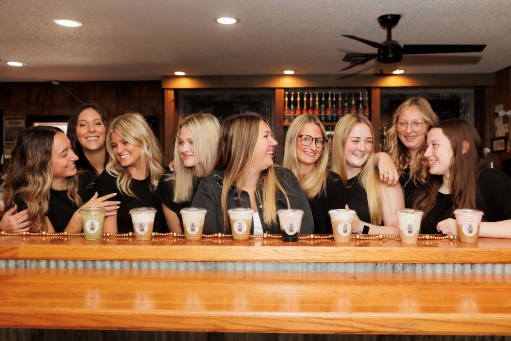 A group of friends enjoying drinks together at a wooden bar counter under warm lighting.