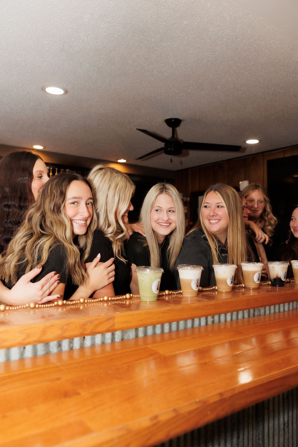 Group enjoying beverages at a rustic bar with wooden countertop and ambient lighting.