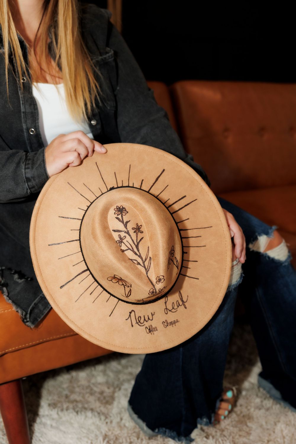 Close-up of a wooden disc with floral design and sunburst pattern held against an orange leather couch.