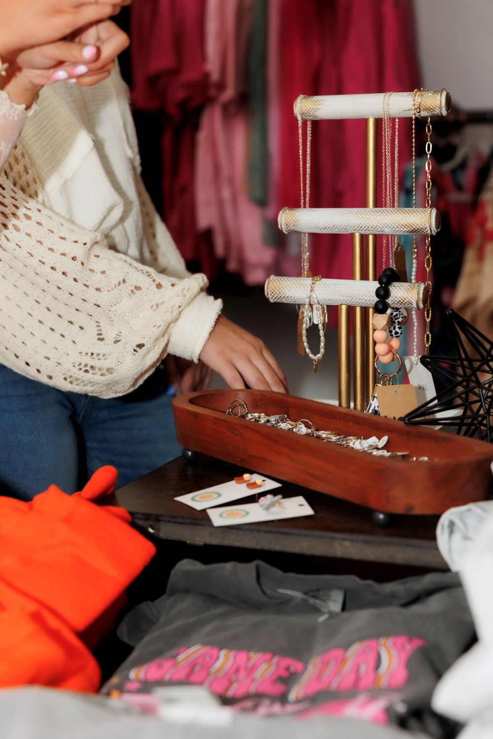 Jewelry display stand with necklaces and accessories next to orange clothing items.