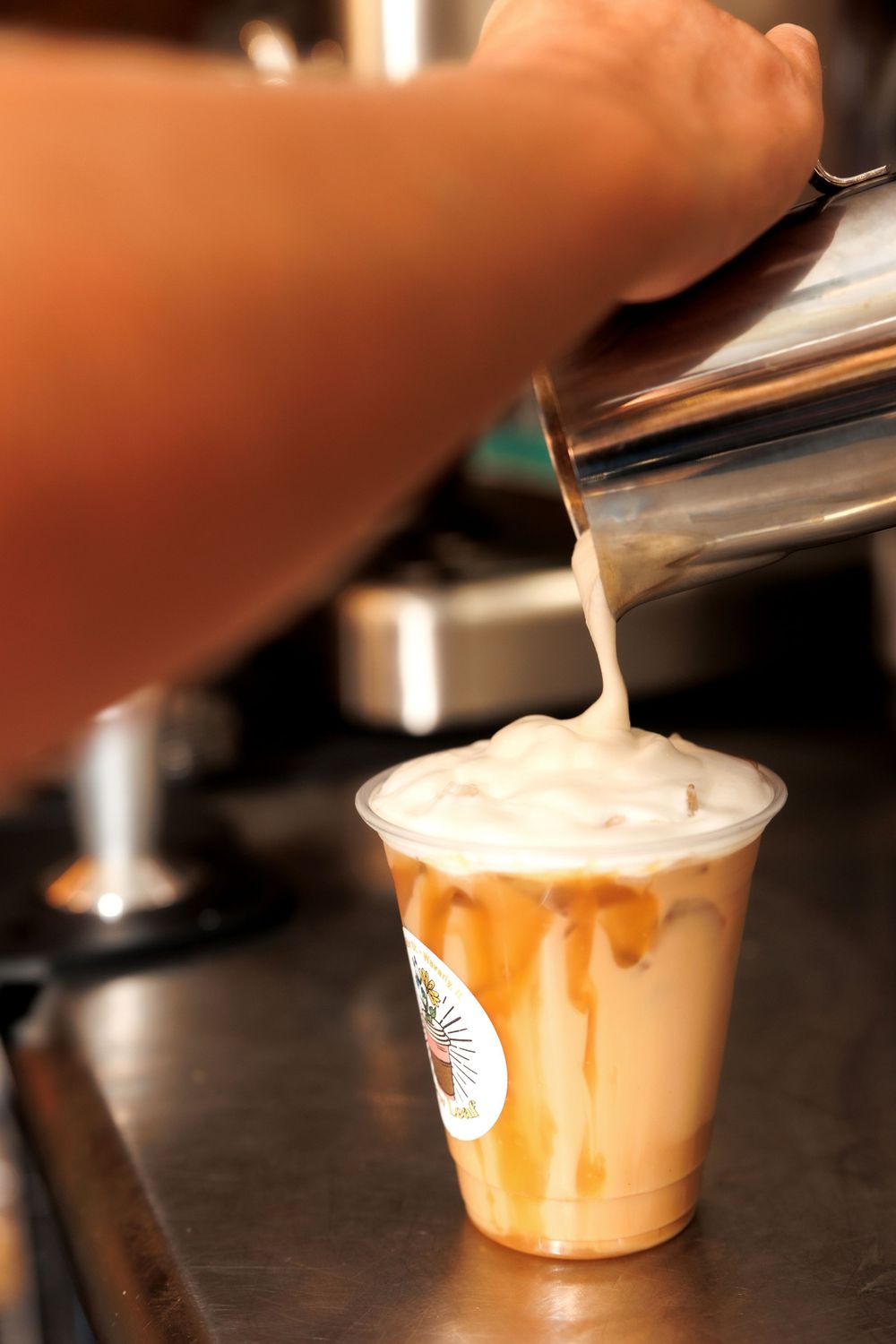 Steamed milk being poured into a caramel-decorated cold drink creating latte art.