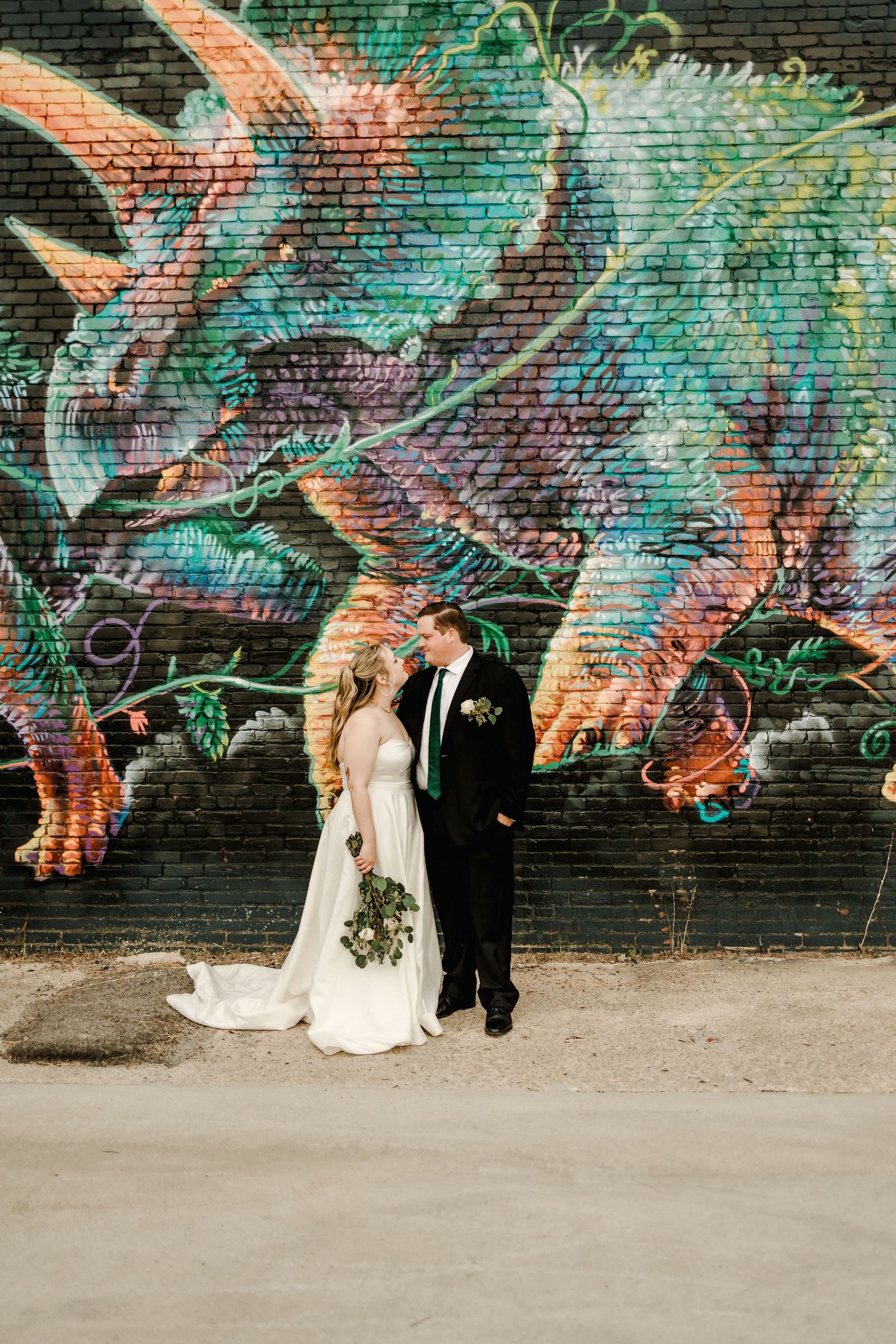 A couple poses against a vibrant street art mural with turquoise and coral tones.