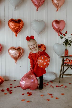 Festive Valentine's scene with heart balloons and decorative red rose petals scattered on floor.