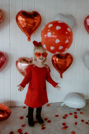 Stylish red Valentine's Day outfit with heart balloons and white wall backdrop.
