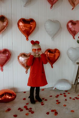 Playful Valentine's pose with red heart balloons and scattered rose petals.