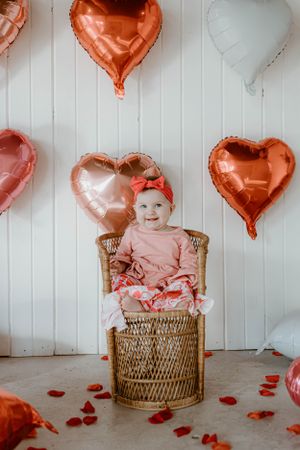 Romantic Valentine's setup with wicker chair and pink heart balloons on white backdrop.