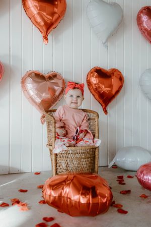 Rose gold and white heart balloons decorate a Valentine's Day themed photo setup with wicker chair.