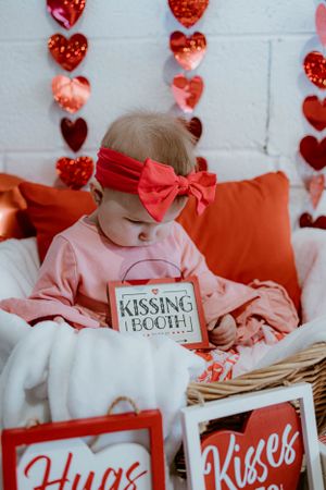 Valentine's theme photo with heart decorations, pink outfit and 'Kissing Booth' sign.