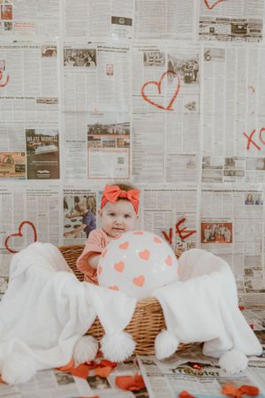 Valentine's themed photo with newspaper wall, heart decorations and wicker basket setting.
