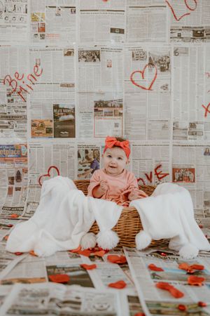 Whimsical Valentine's setup featuring wicker basket against newspaper wall with red heart decorations.