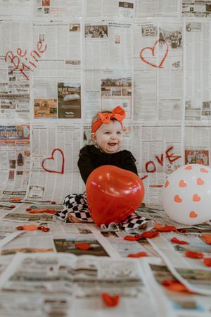 Valentine's themed photo with heart balloons and newspaper wall background.