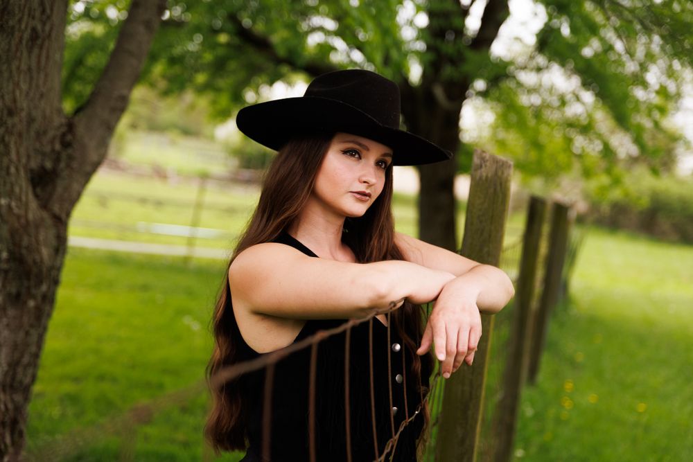 Dramatic portrait in western wear leaning on wooden fence at golden hour.