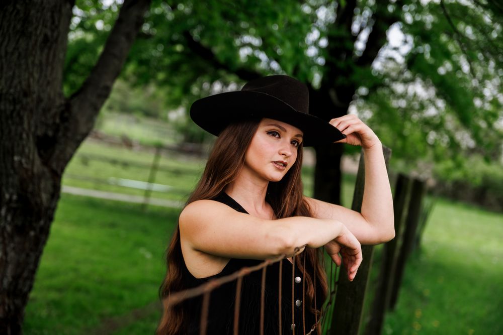 Stylish western fashion portrait with black hat against pastoral backdrop.