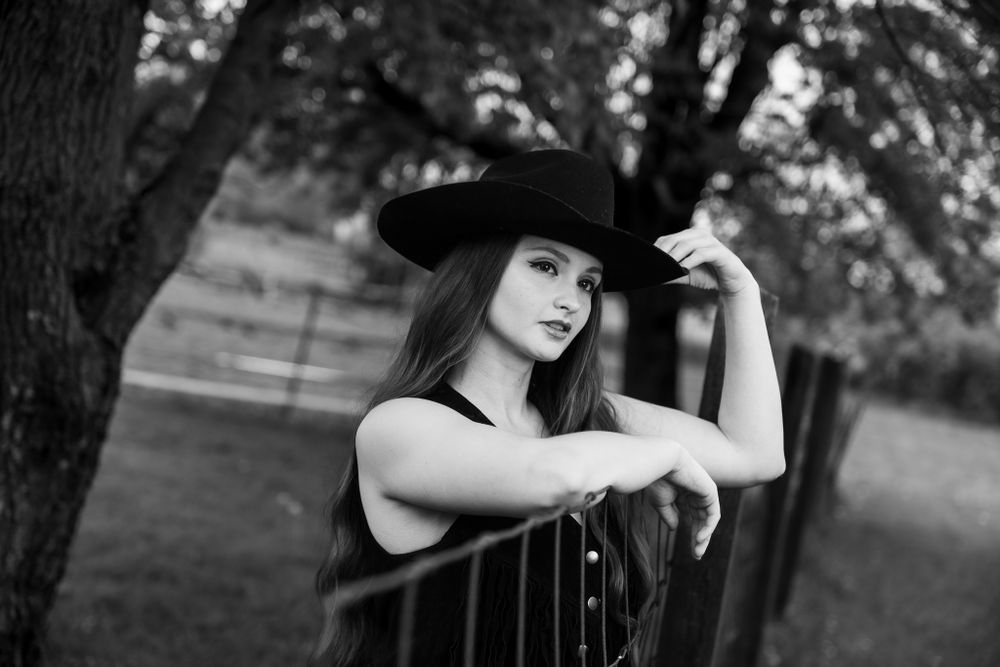 Black and white portrait in western attire against rustic fence.