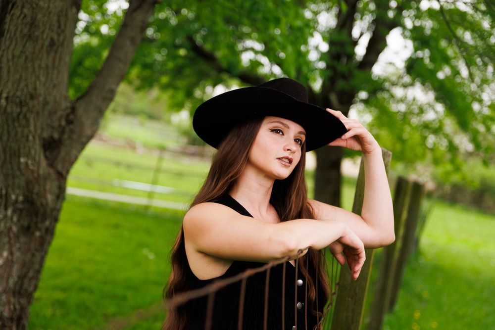 Dramatic outdoor portrait in western wear with sunlit pastoral background.