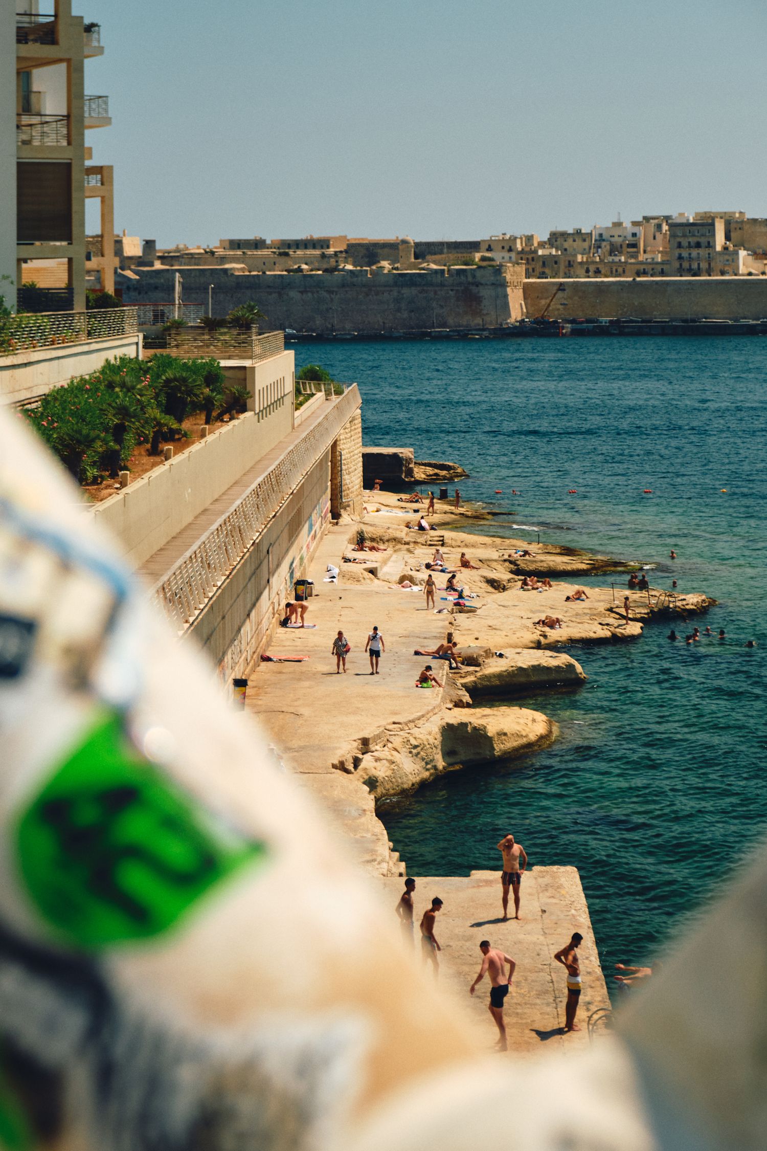 Swimmers and sunbathers enjoying a rocky beach along Malta's blue Mediterranean coastline.
