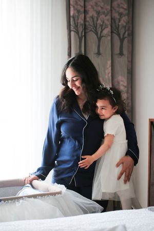 Joyful mother and child sharing a warm embrace near window with tree-patterned curtains.