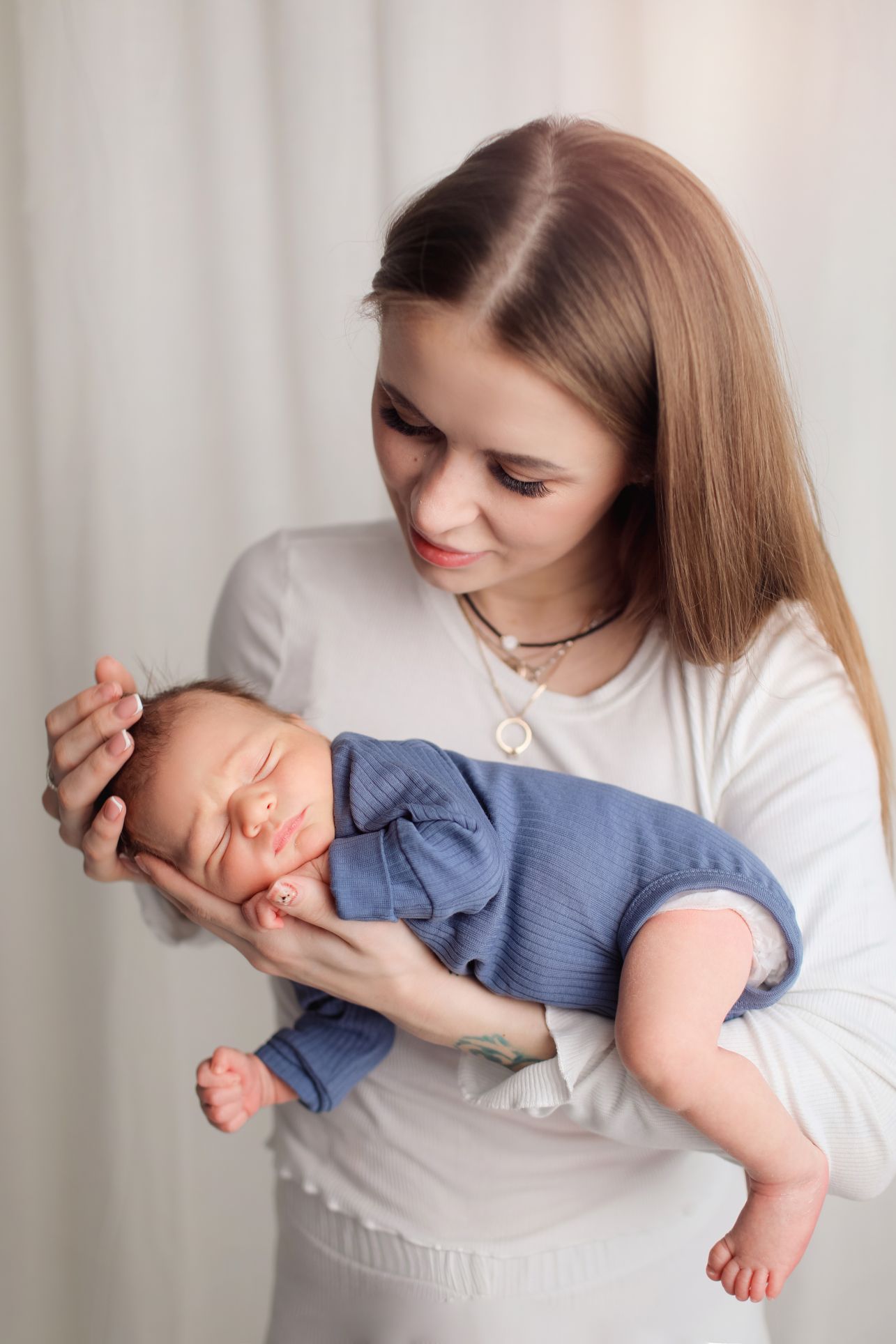 A peaceful newborn in blue clothing sleeping in caring arms.