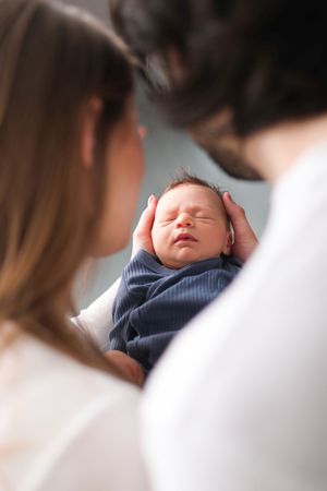 A sleeping newborn being cradled lovingly against a light background.