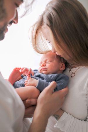 A sleeping infant in blue clothing being held tenderly by caregivers.