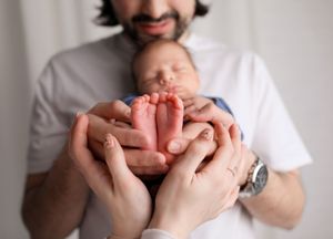 Gentle hands holding tiny newborn feet against a light background.