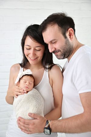 A sleeping newborn baby swaddled in beige cloth is held tenderly against a white background.