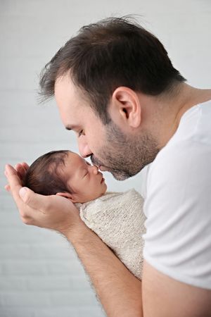 A tender moment with a newborn baby wrapped in soft beige fabric against a light gray background.