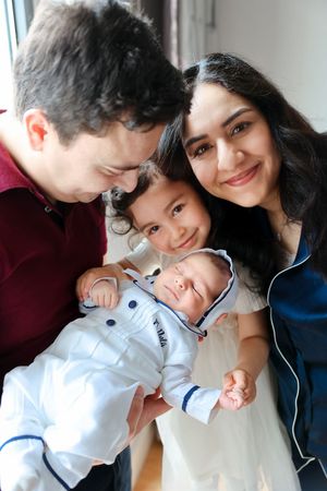 A family gathering close together while holding a baby dressed in white nautical-style clothing.