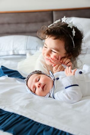 A sweet moment between siblings as one admires a sleeping baby on blue bedding.