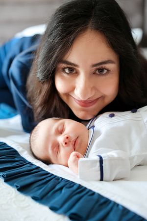A sleeping baby in white nautical outfit rests peacefully on blue bedding.